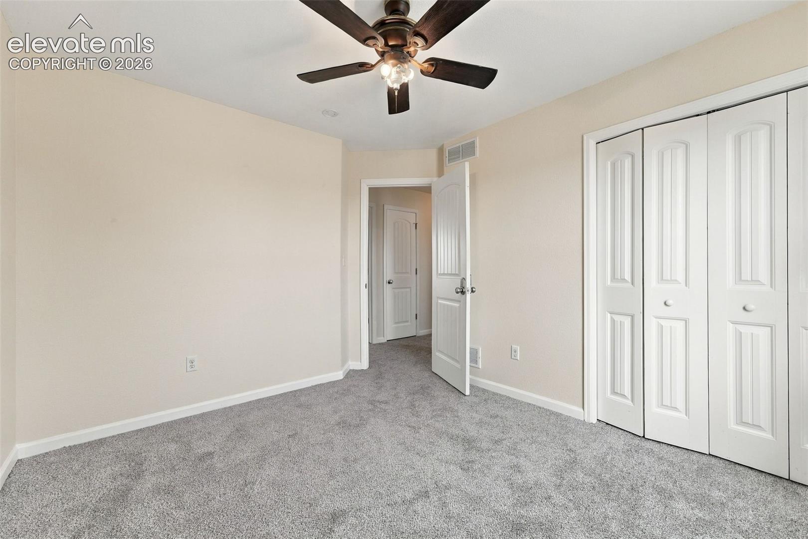Neutral-toned wall paint, wall-to-wall carpeting, ceiling fan with integrated lighting, and white multi-panel doors