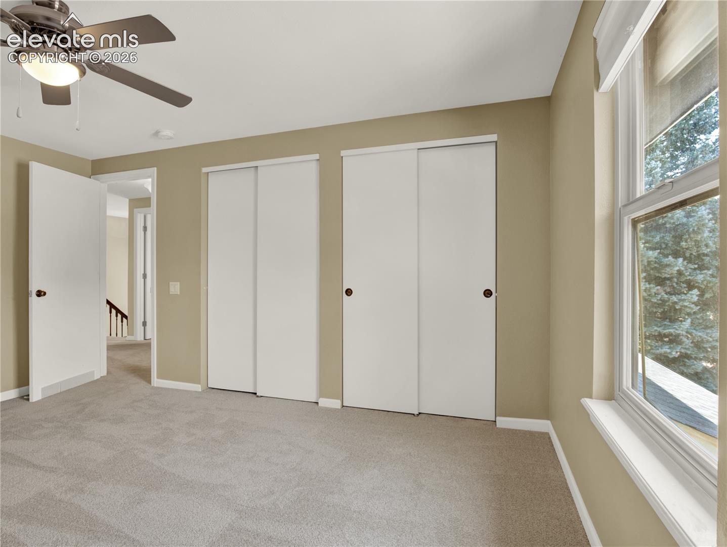 Room featuring neutral wall tones, wall-to-wall carpeting, dual sliding-door closets, and a ceiling fan with integrated lighting