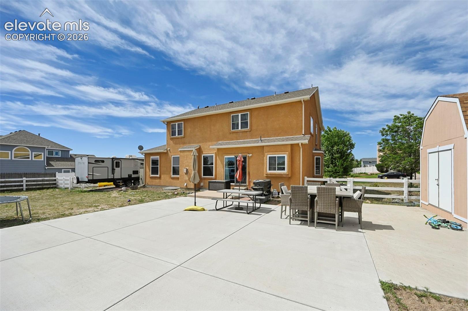 Expansive concrete patio with stucco exterior, rear double doors, multiple windows, and a detached storage shed