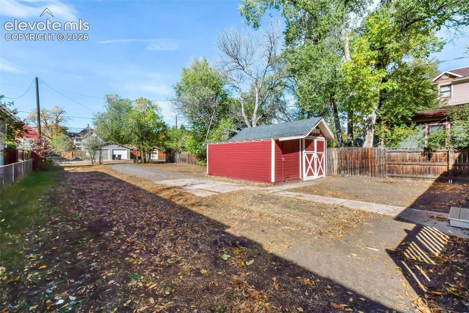Spacious backyard featuring a detached storage shed, wood fencing, concrete pathways, and mature trees