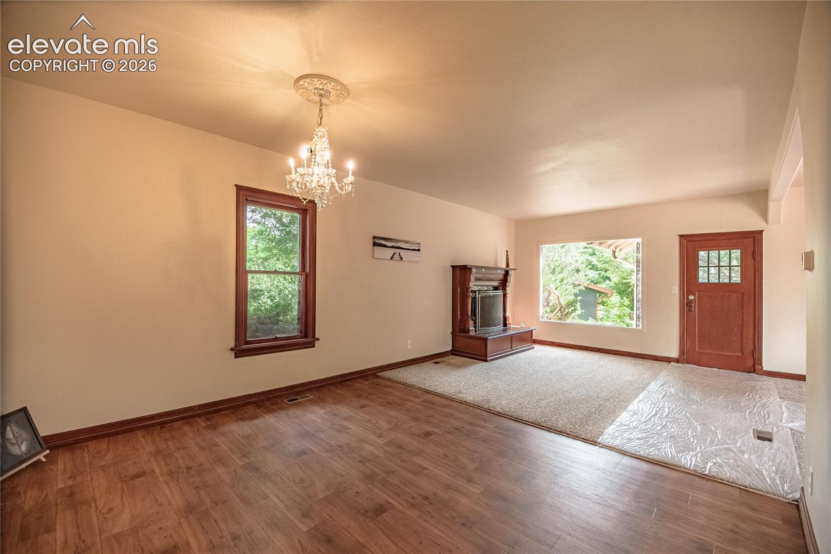 Wood-finish flooring with a complementary carpeted area, multiple windows with wood trim, built-in media console, and an entry door with a multi-pane window