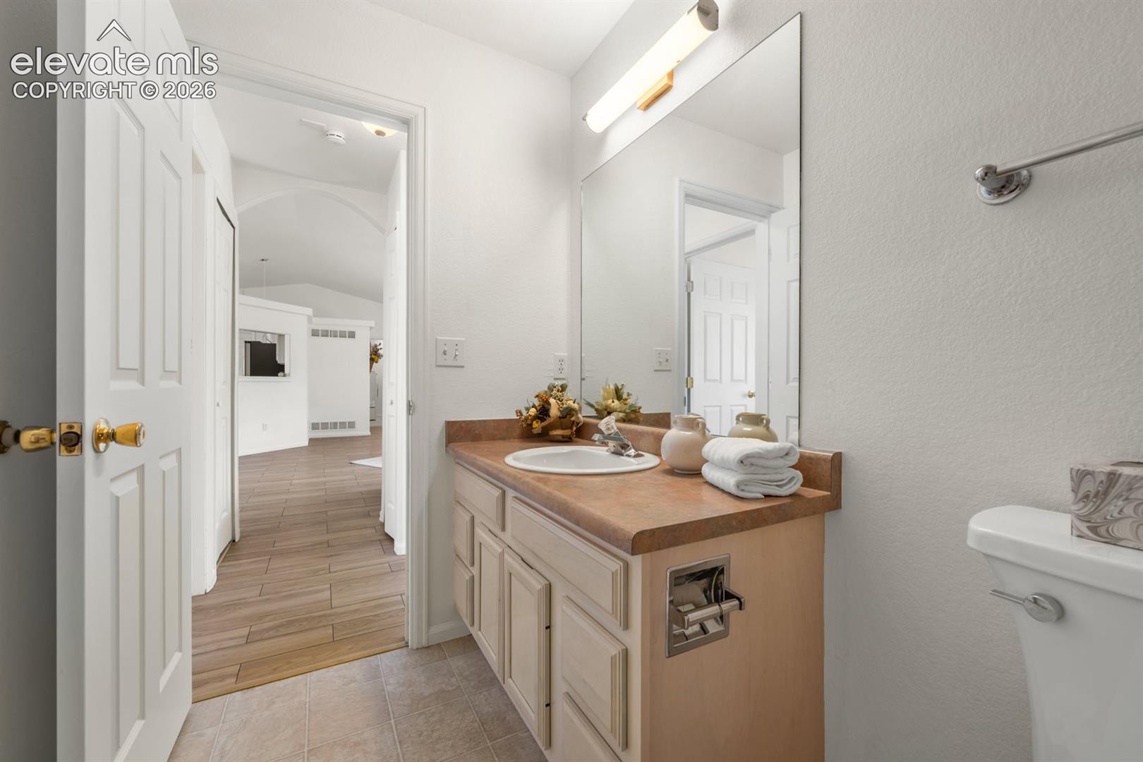 Bathroom vanity featuring a light-wood finish cabinet, rounded vessel-style sink, solid-surface countertop, full-width wall mirror, and integrated lighting