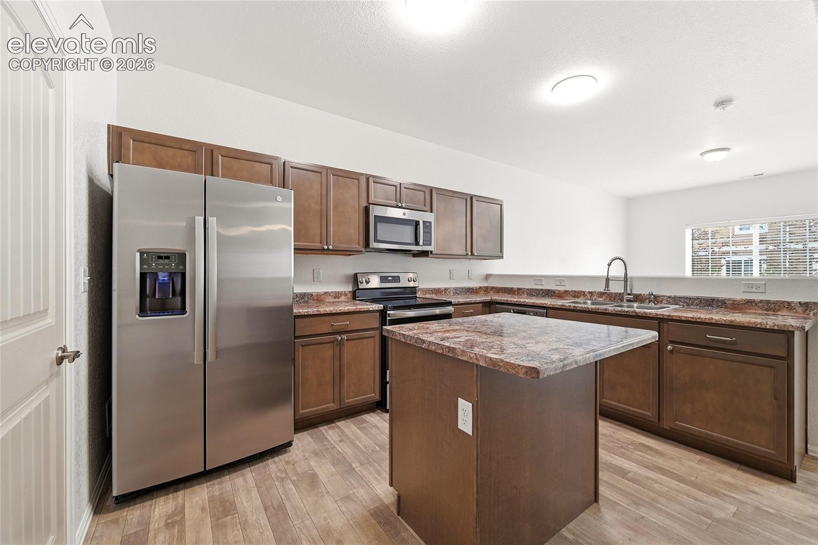 Kitchen featuring wood cabinetry, stone-finish countertops, stainless steel refrigerator, built-in microwave, and wood-finish flooring