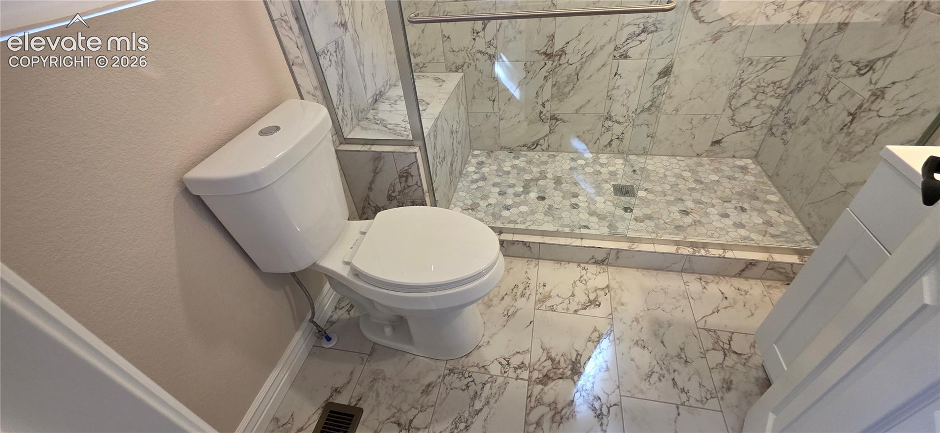 Walk-in shower with clear glass enclosure, a built-in shower bench, and hexagonal mosaic tile flooring