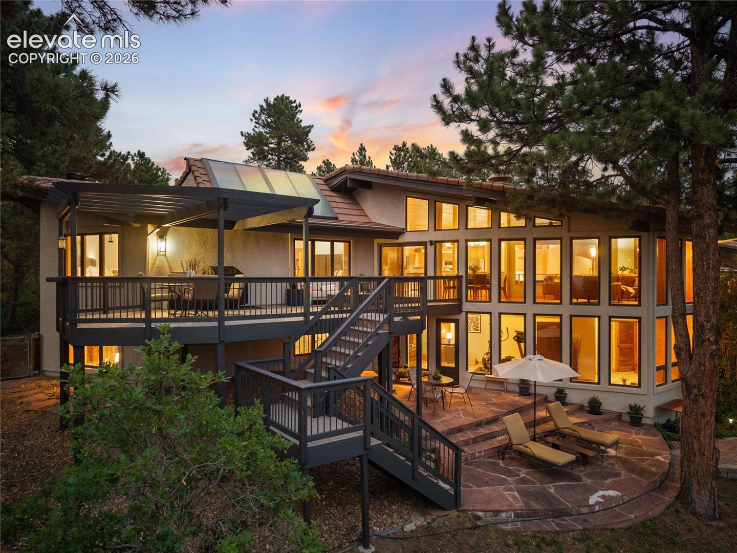 Multi-level rear exterior featuring a large upper deck with a pergola, a curved flagstone patio, and extensive window walls