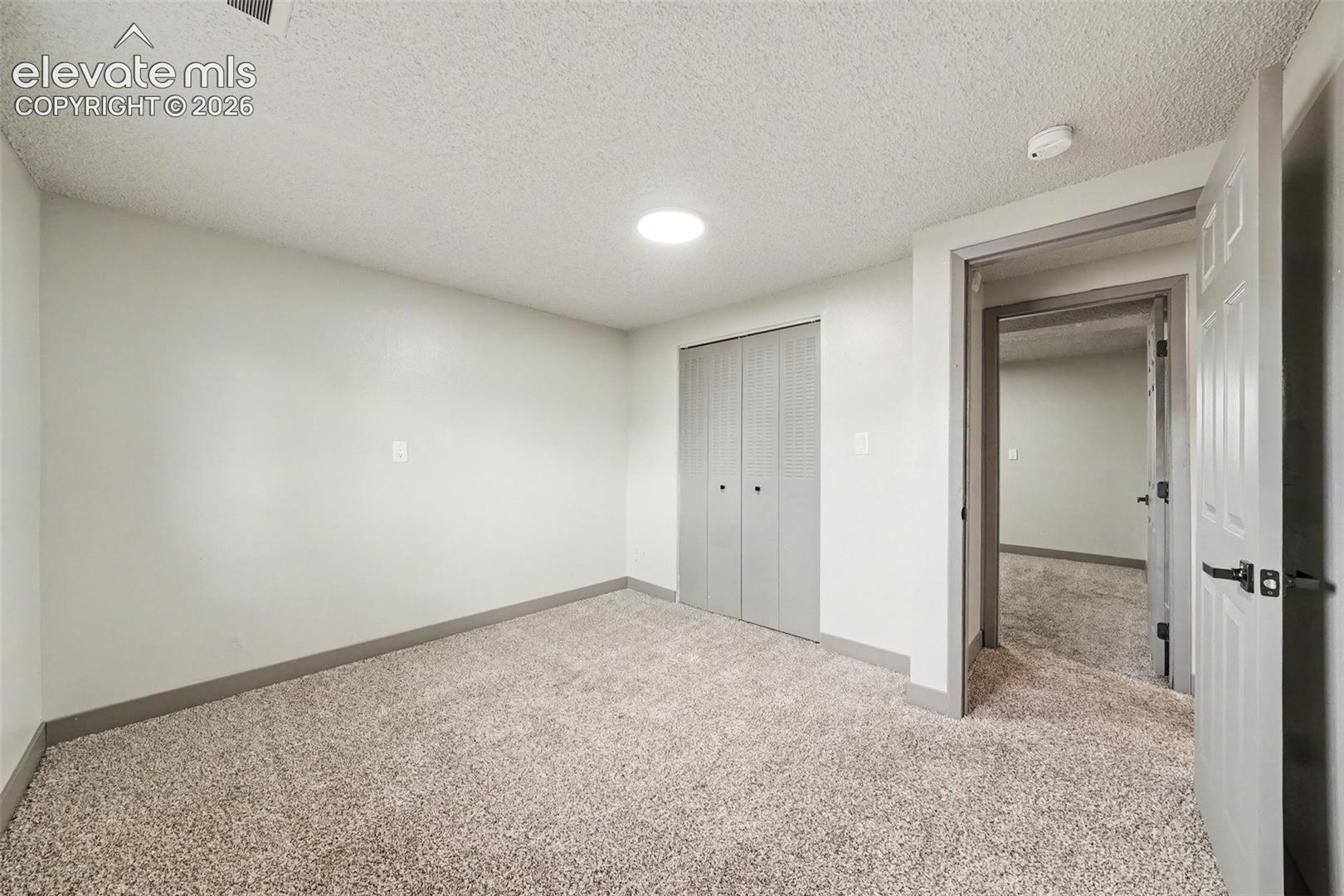 Interior space featuring neutral wall tones, wall-to-wall carpeting, bi-fold closet doors, and a six-panel door with matte black hardware