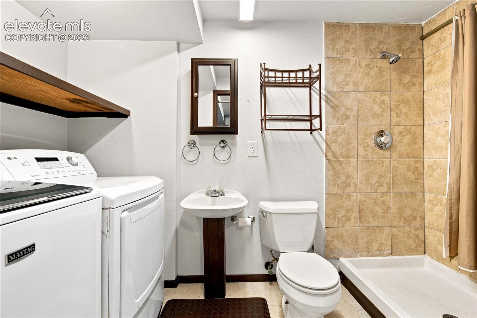 Full bathroom featuring a ceramic tile shower, white pedestal sink, and a floating wood-finish shelf