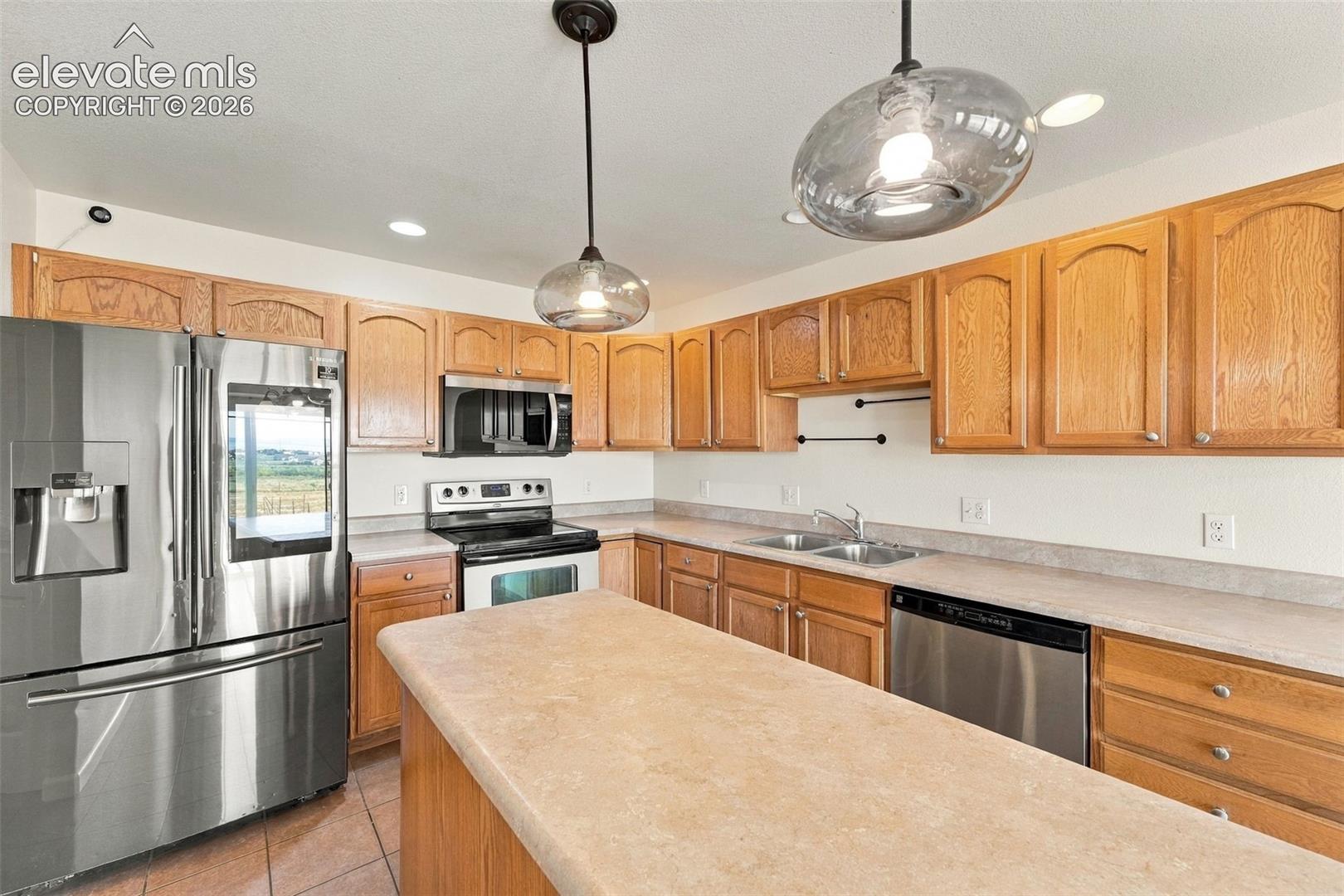 Kitchen featuring medium-tone wood cabinetry, stainless steel appliances, solid-surface countertops, dual pendant lighting, and tile flooring
