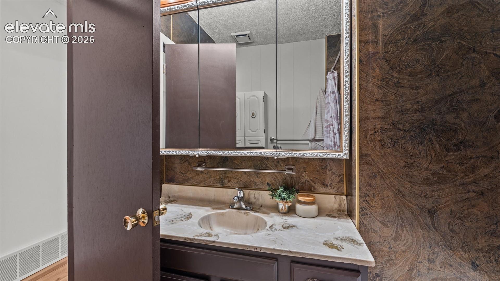 Spa-inspired bathroom vanity featuring a ceramic sink set within a wood-finish countertop, illuminated by a large framed mirror with integrated LED lighting