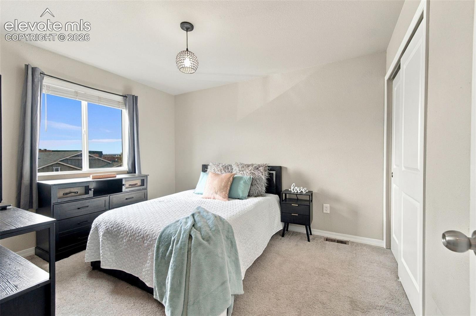 Neutral-toned bedroom featuring wall-to-wall carpeting, a dual-panel closet door, and a single-light pendant fixture