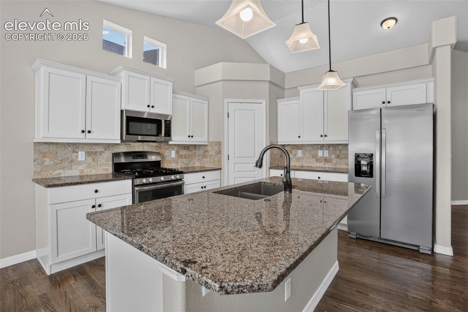 Kitchen featuring an island with an undermount sink, granite countertops, white cabinetry, and stainless steel appliances
