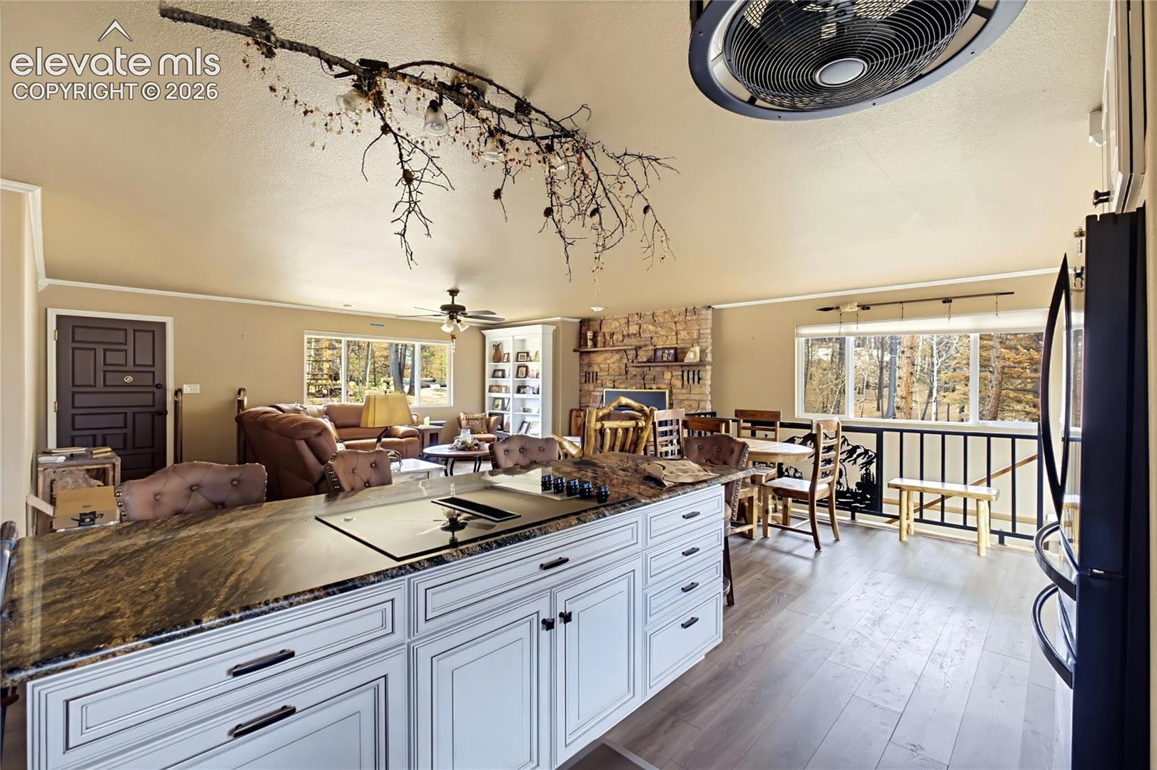 Kitchen featuring a white cabinetry island with dark natural stone surfacing, integrated cooktop, wood-finish flooring, floor-to-ceiling stone fireplace, and custom built-in shelving
