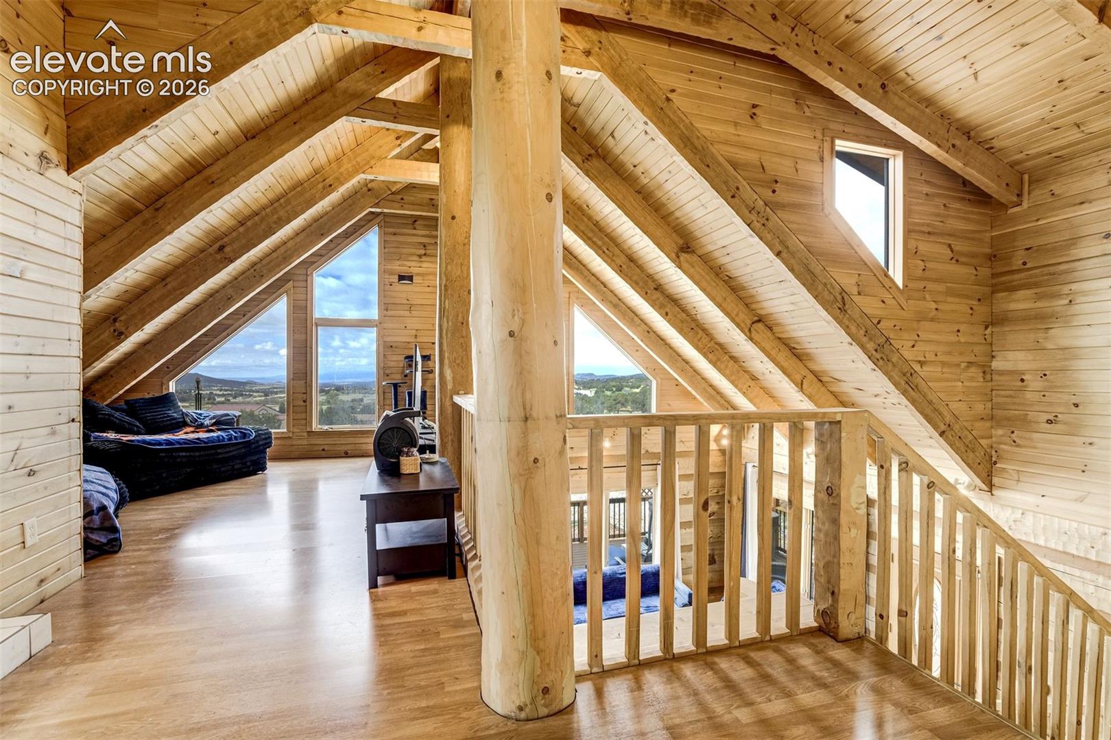 Vaulted ceiling with exposed wood beams, natural wood-finish flooring, and triangular windows providing expansive outdoor scenery