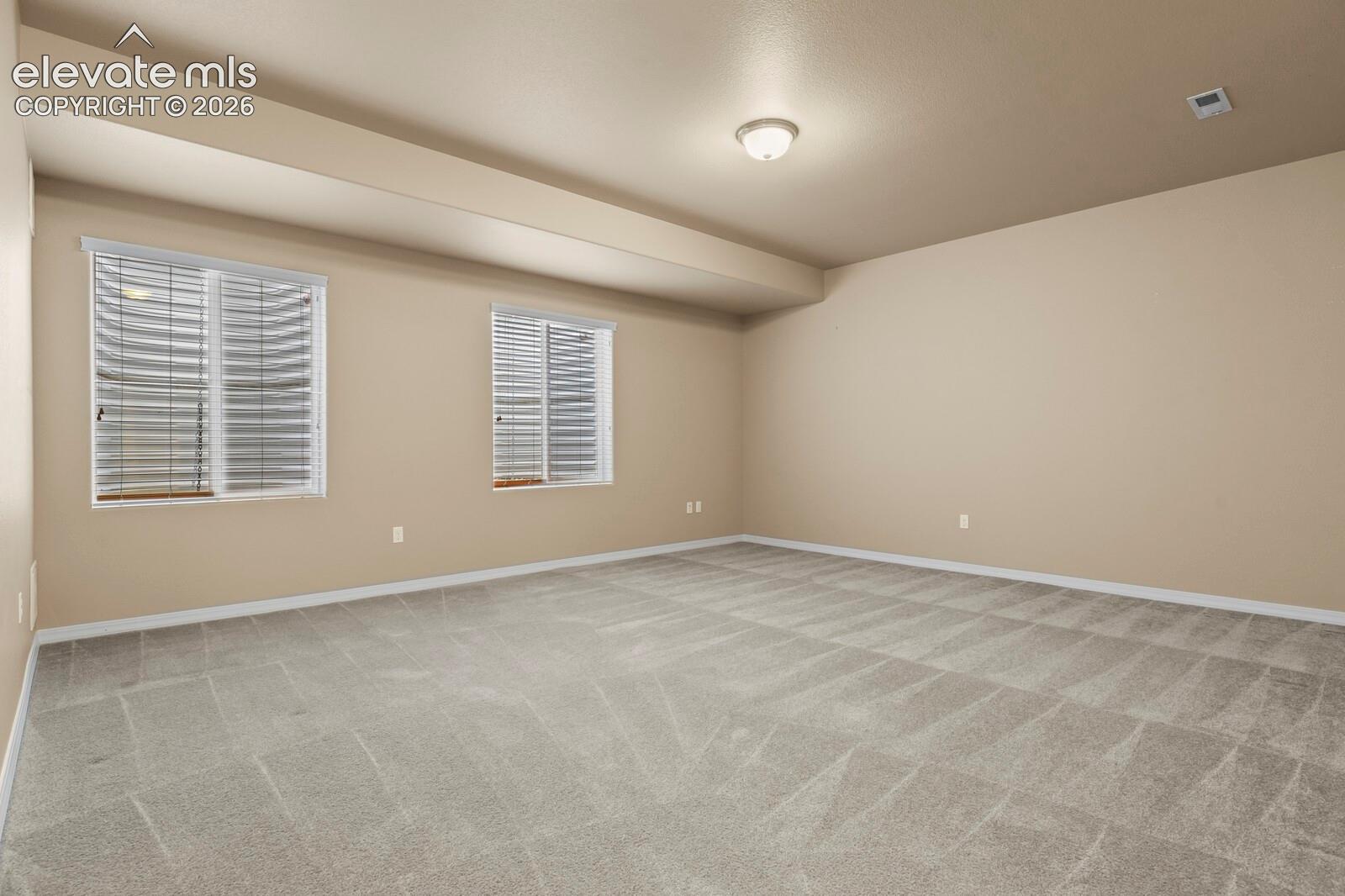 Expansive room featuring neutral wall tones, two windows with blinds, a flush mount ceiling light, and patterned carpeting