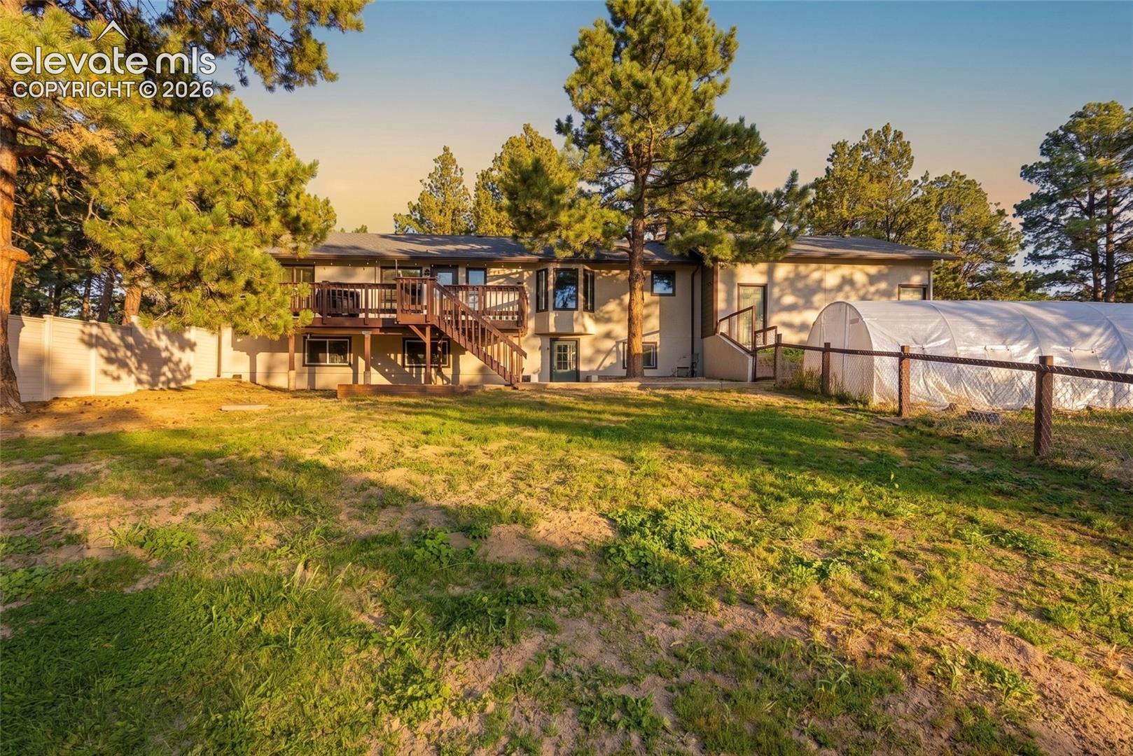 Expansive grassy yard with mature trees, a wood deck with stairs, a partial privacy fence, and fenced area for pets