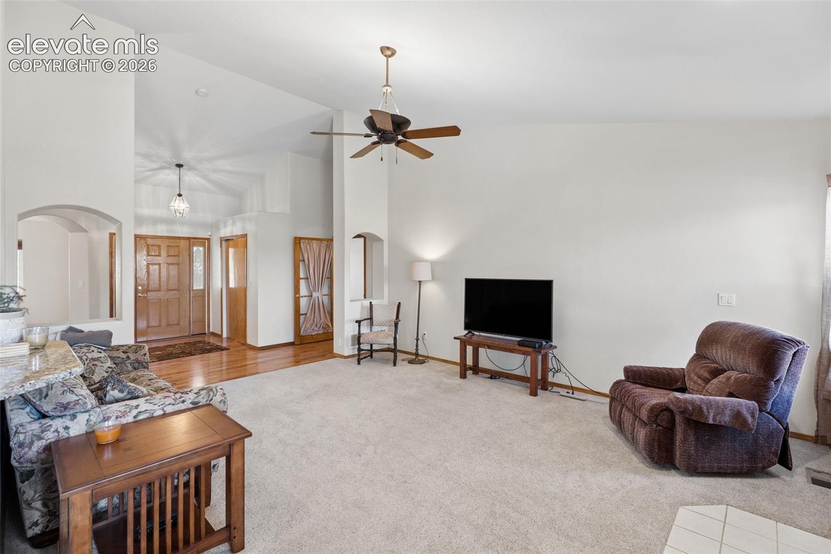 Vaulted ceilings, architectural archways, wood-finish flooring, and a ceiling fan with integrated lighting