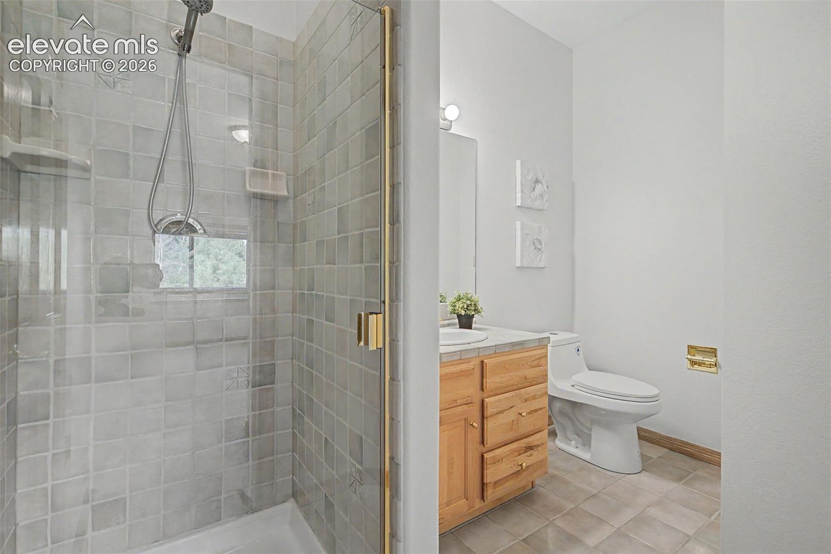 Shower with glass enclosure, gold-toned hardware, and square tile surround