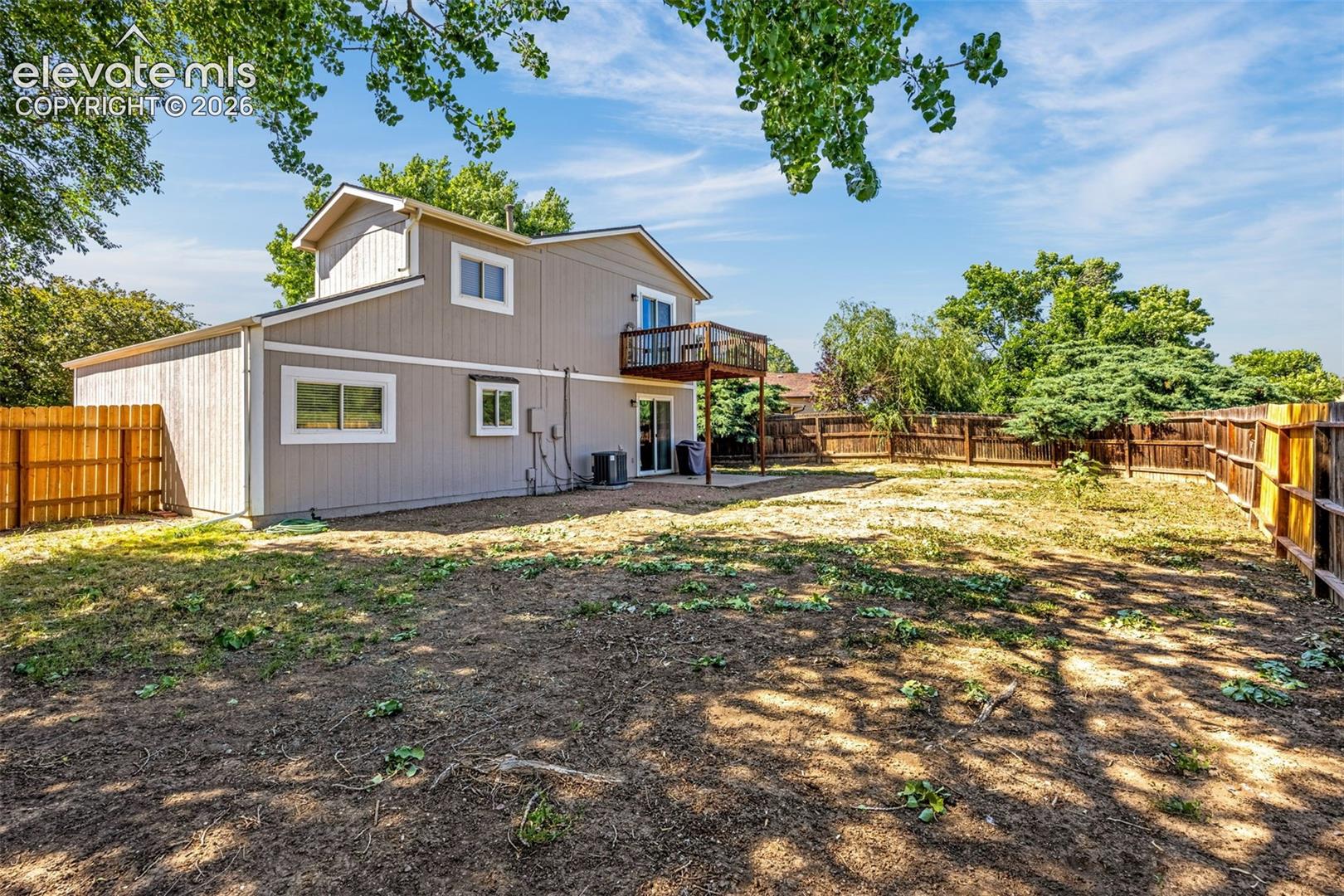 Two-story exterior with wood siding, elevated wooden deck, sliding glass door, and full perimeter wood fencing