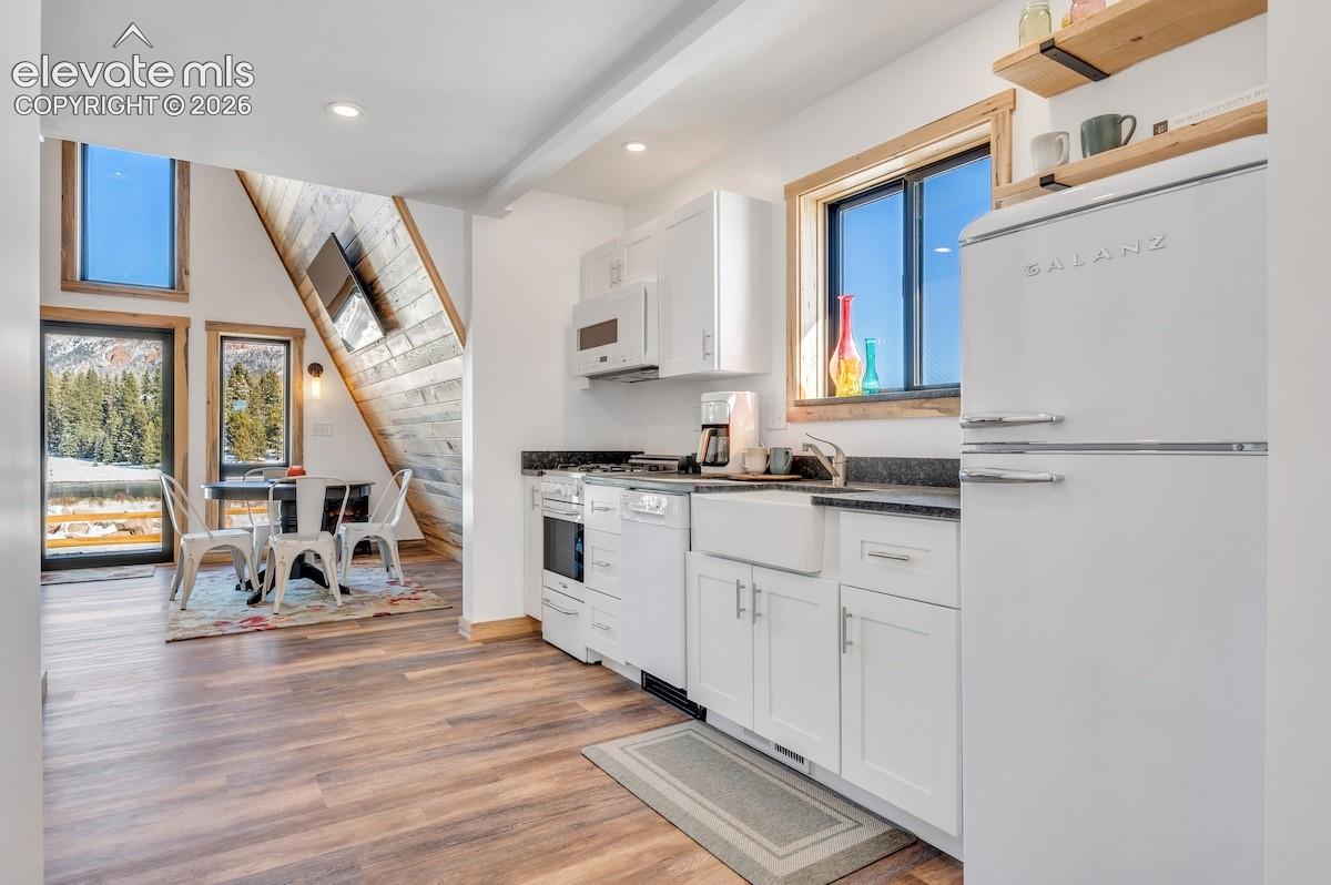 Kitchen featuring white cabinetry, apron-front sink, dark stone-finish countertops, and wood-finish flooring, complemented by an A-frame architectural design with wood-paneled wall accents