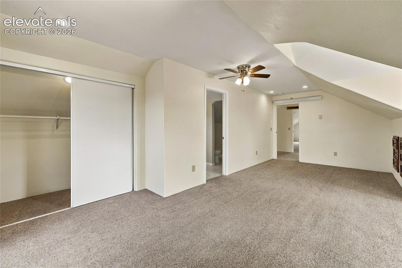 Sloped ceiling architecture featuring recessed lighting, a ceiling fan with integrated light kit, wall-to-wall carpeting, and a closet with sliding doors