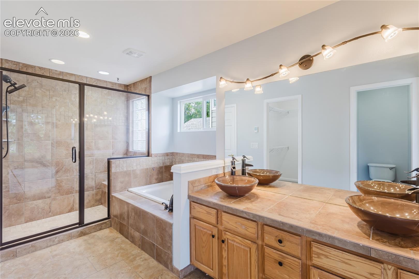 Spacious bath featuring a walk-in shower with tile surround, built-in soaking tub, dual vessel sinks, and a large vanity with wood cabinetry