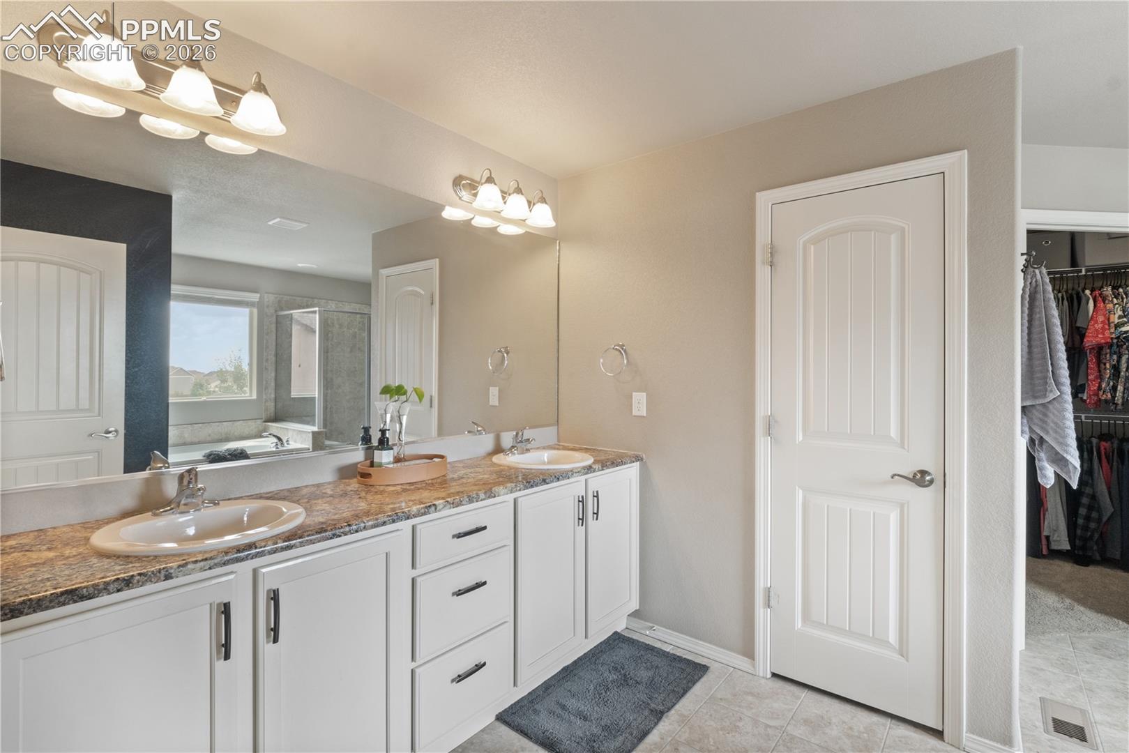 Bathroom with double vanity, a shower stall, a walk in closet, a bath, and light tile patterned floors