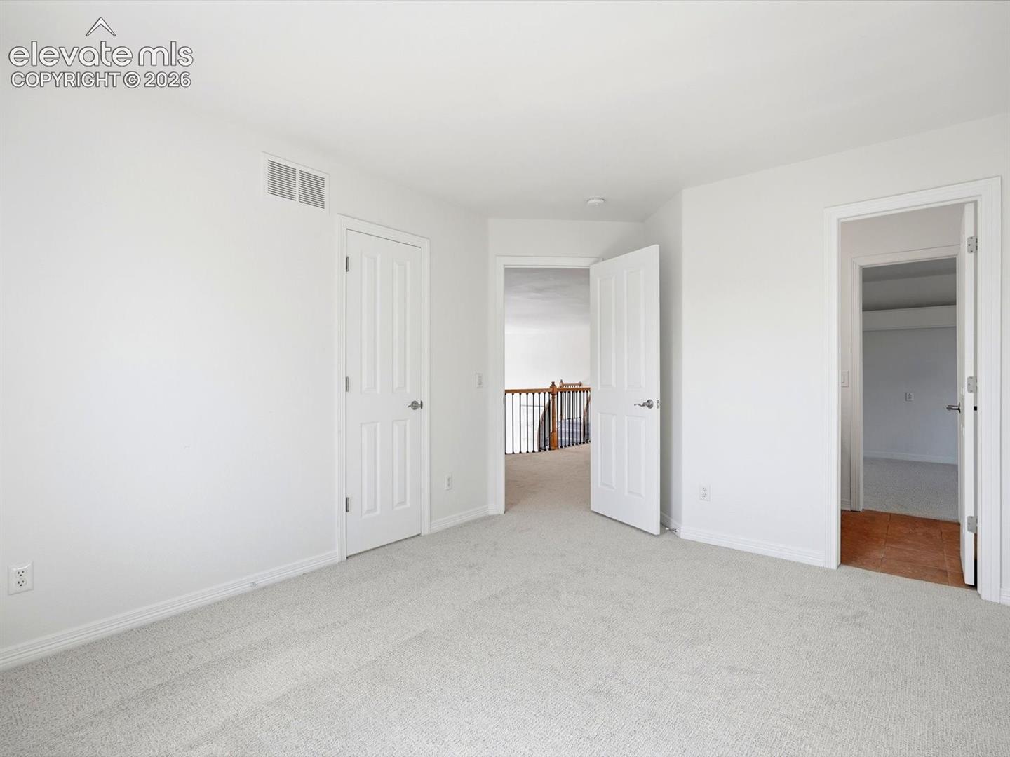 Interior space featuring neutral carpeting, white walls, six-panel interior doors, and access to a wooden staircase railing