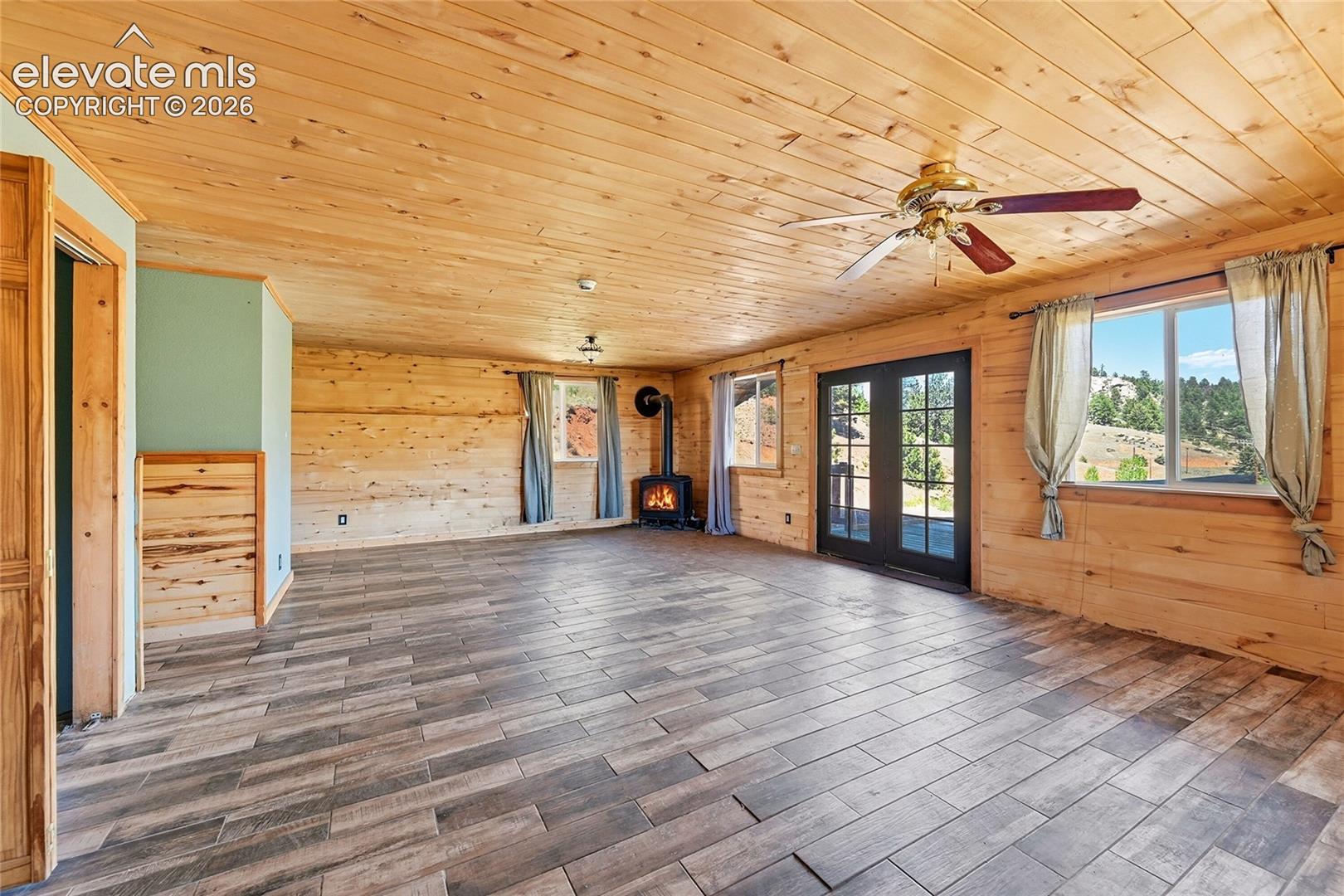 Wood-finish plank flooring, wood-paneled walls, wood-paneled ceiling, ceiling fan, and black French doors