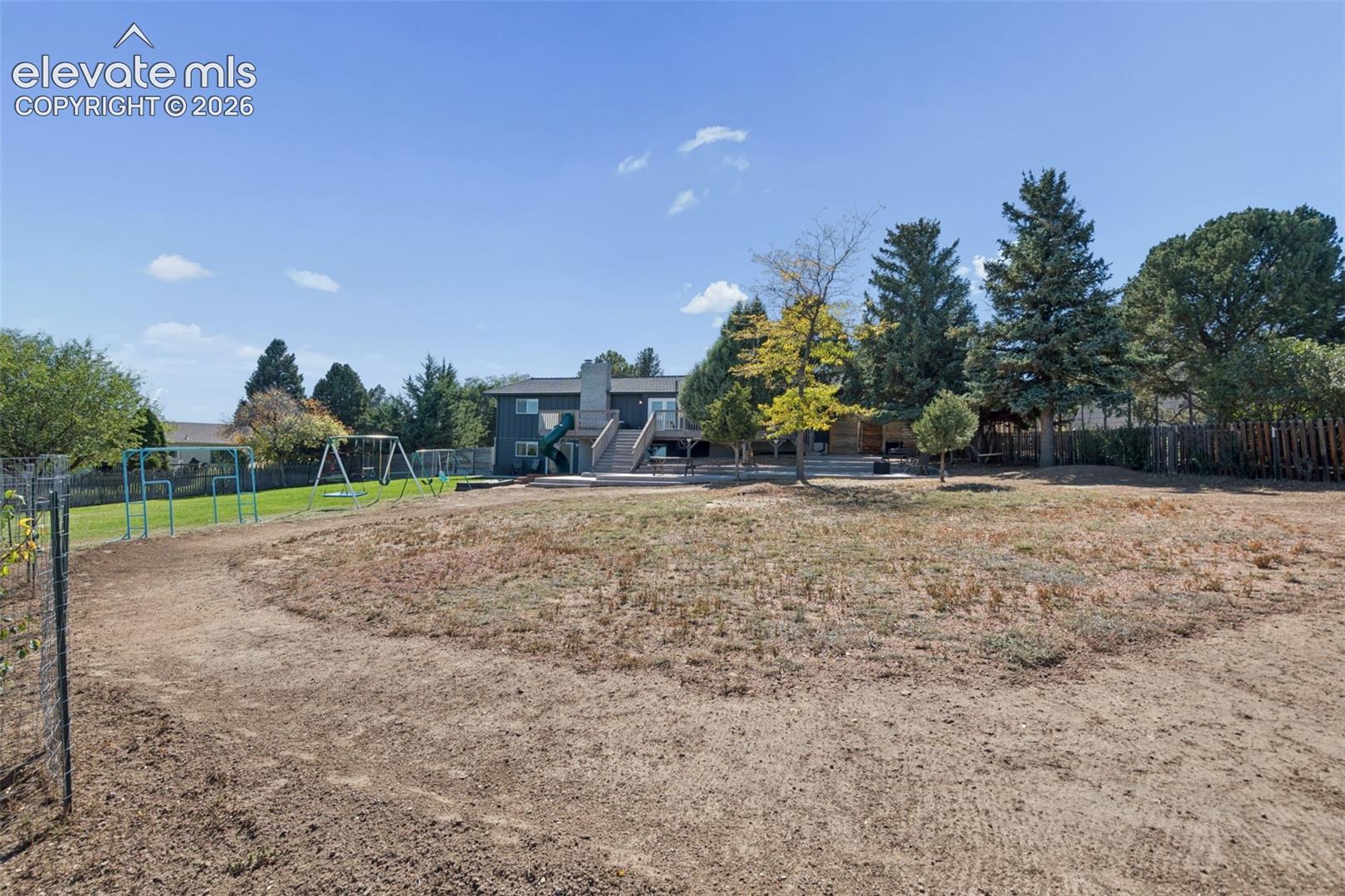Expansive backyard featuring a multi-level wooden deck, stone-paved patio, mature trees, and perimeter fencing