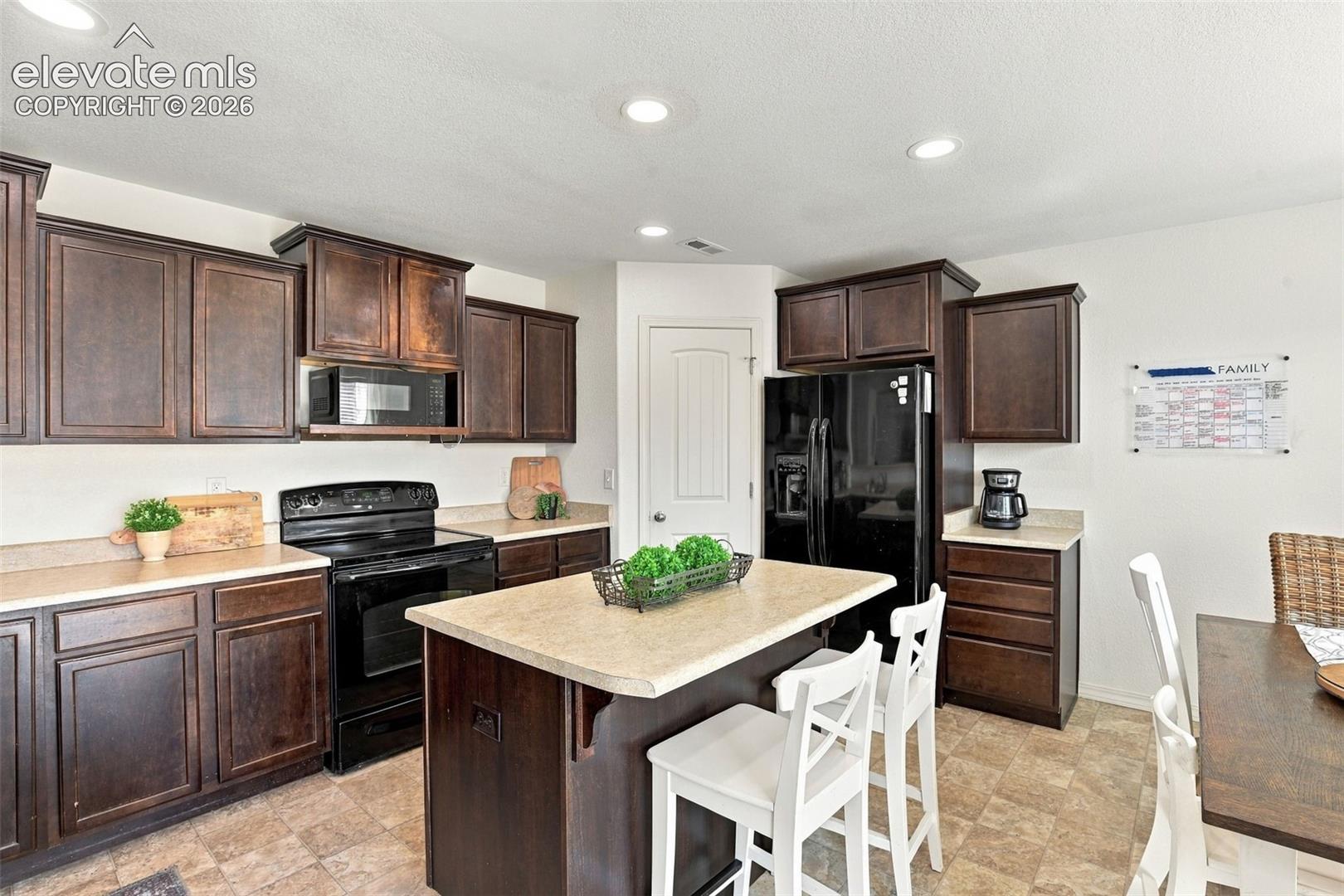Kitchen featuring dark wood cabinetry, a central island with countertop seating, a built-in microwave, an electric range, and a full-size black refrigerator