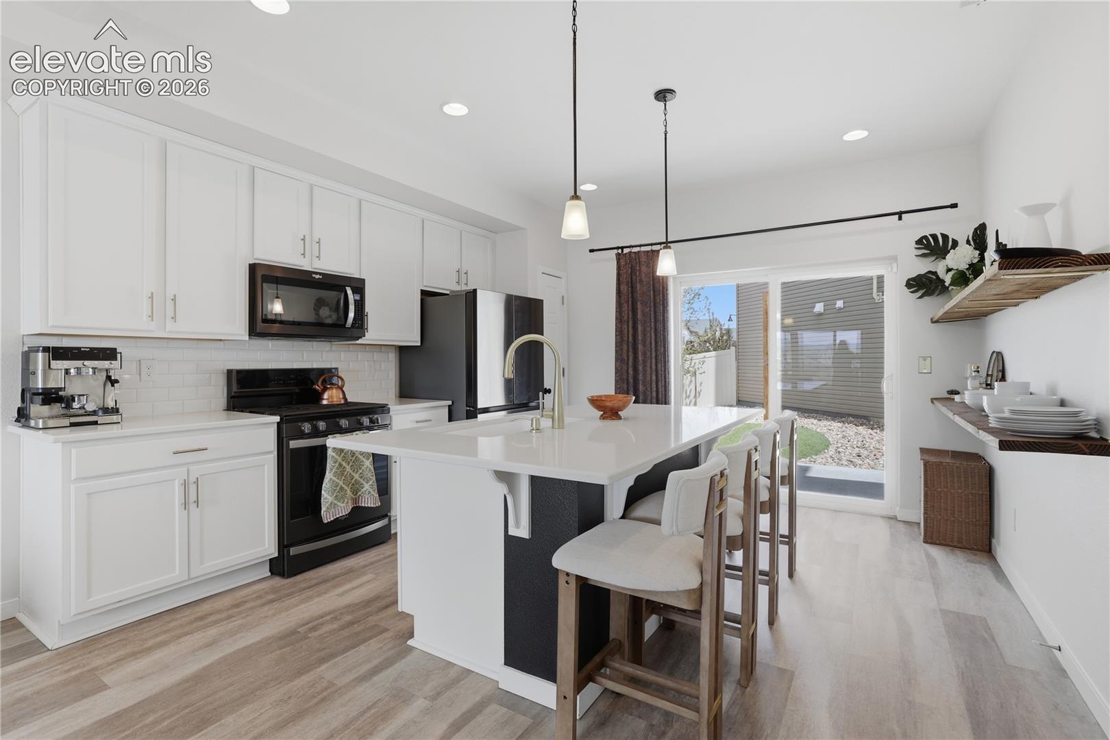 Contemporary kitchen featuring white cabinetry, a central island with countertop seating, stainless steel appliances, wood-finish flooring, and a sliding glass door leading to an outdoor space