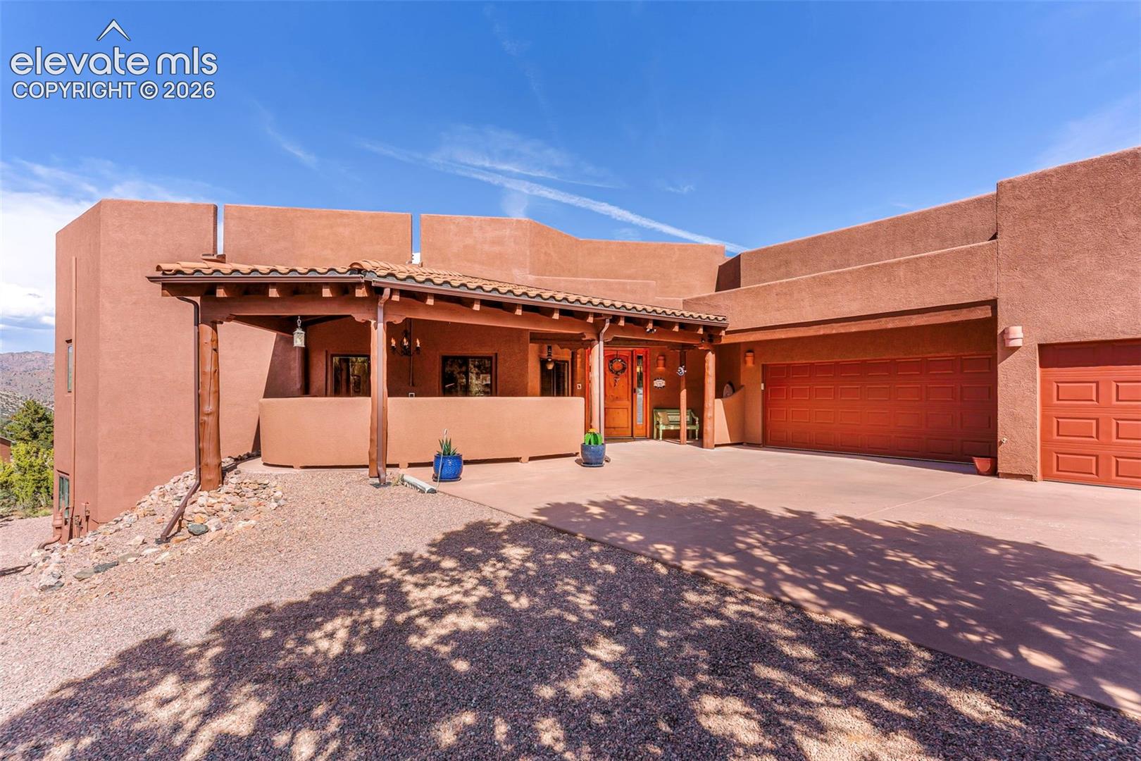 Stucco exterior featuring a covered entryway with timber support beams, clay tile roof accents, and an attached multi-car garage