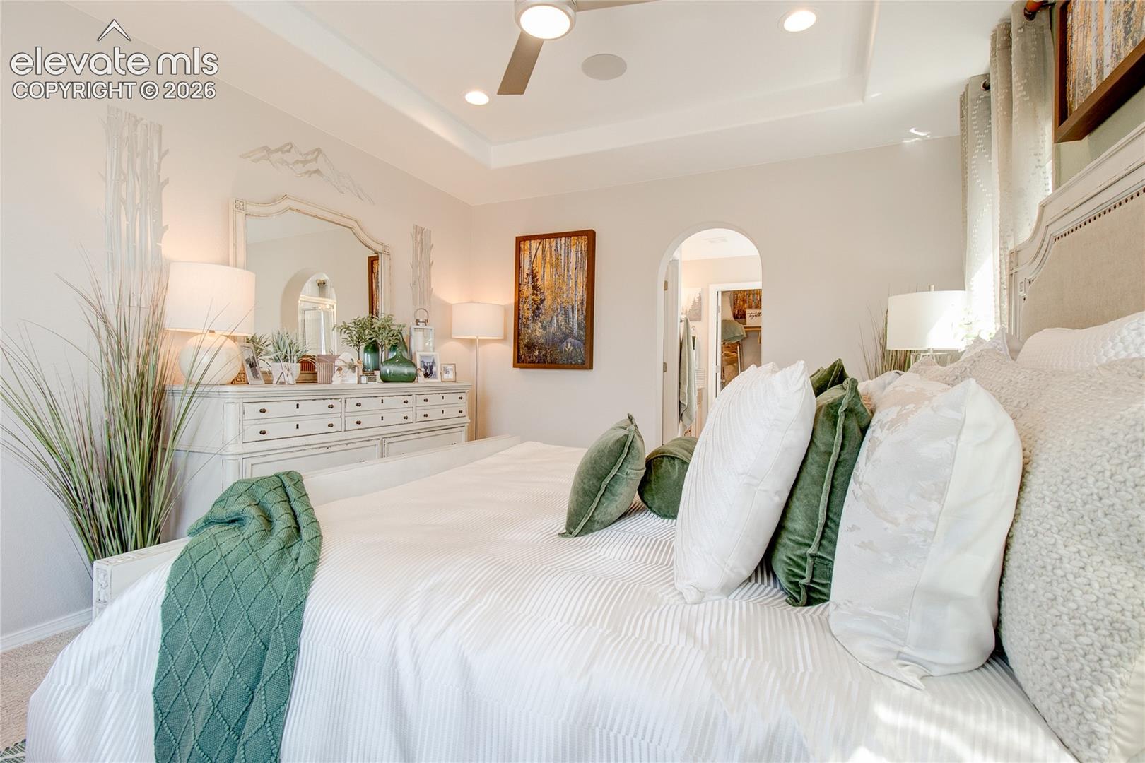 Tray ceiling featuring recessed lighting and a central ceiling fan, arched doorway, and neutral wall color