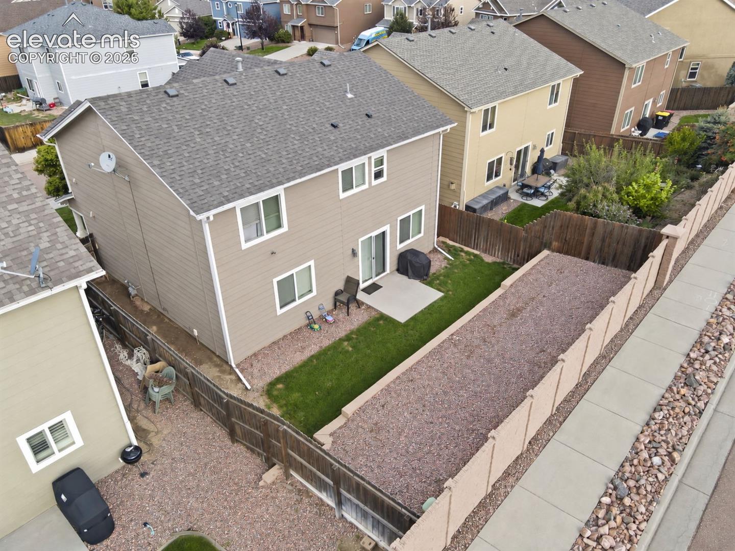 Two-story property with a gravel roof, tan siding, and a concrete patio