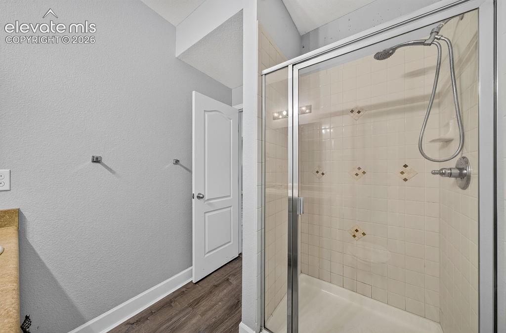 Glass-enclosed shower with a tiled surround, handheld shower fixture, and built-in shelving