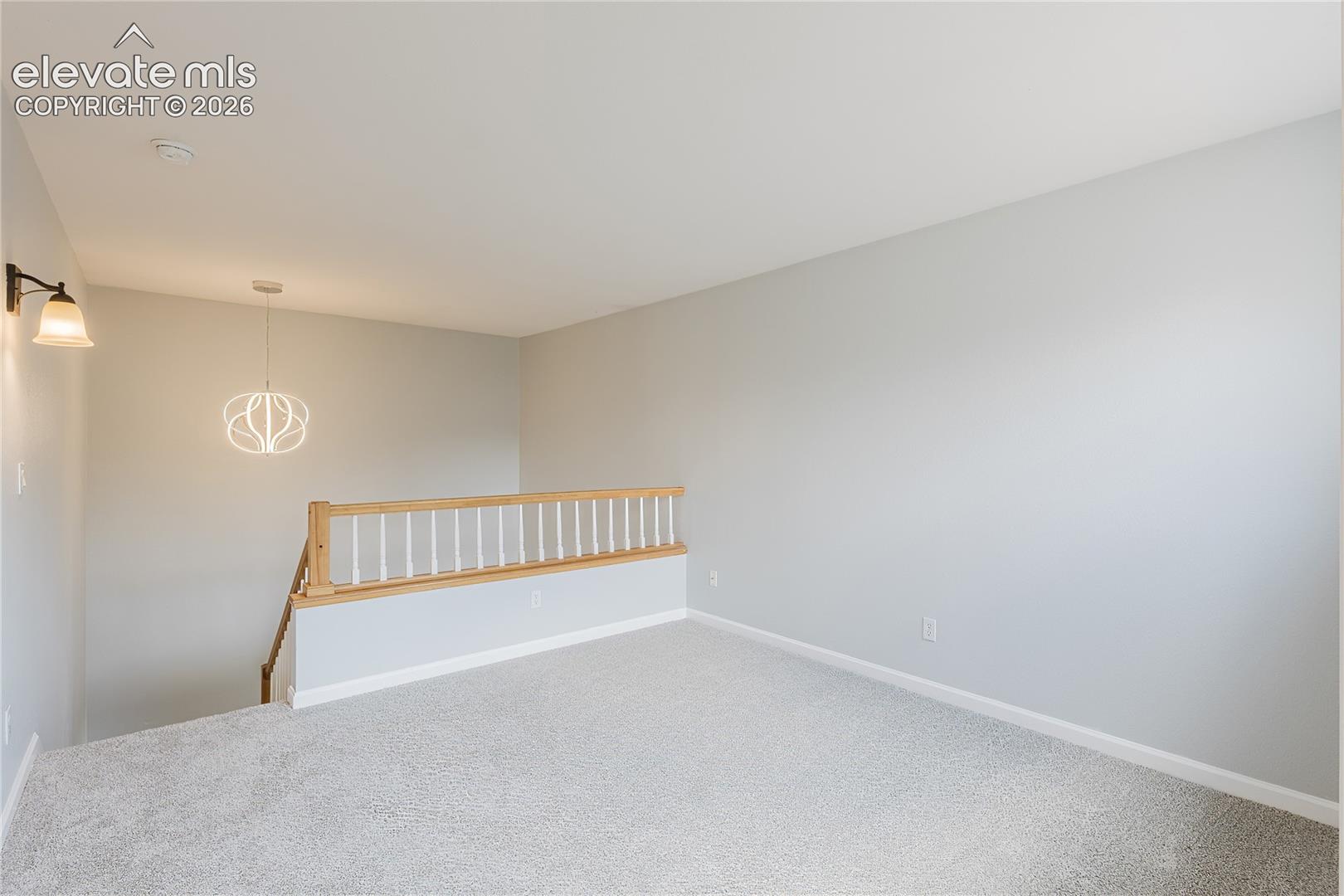 Carpeted loft area with a wood and white spindle railing, modern pendant light fixture, and wall sconce