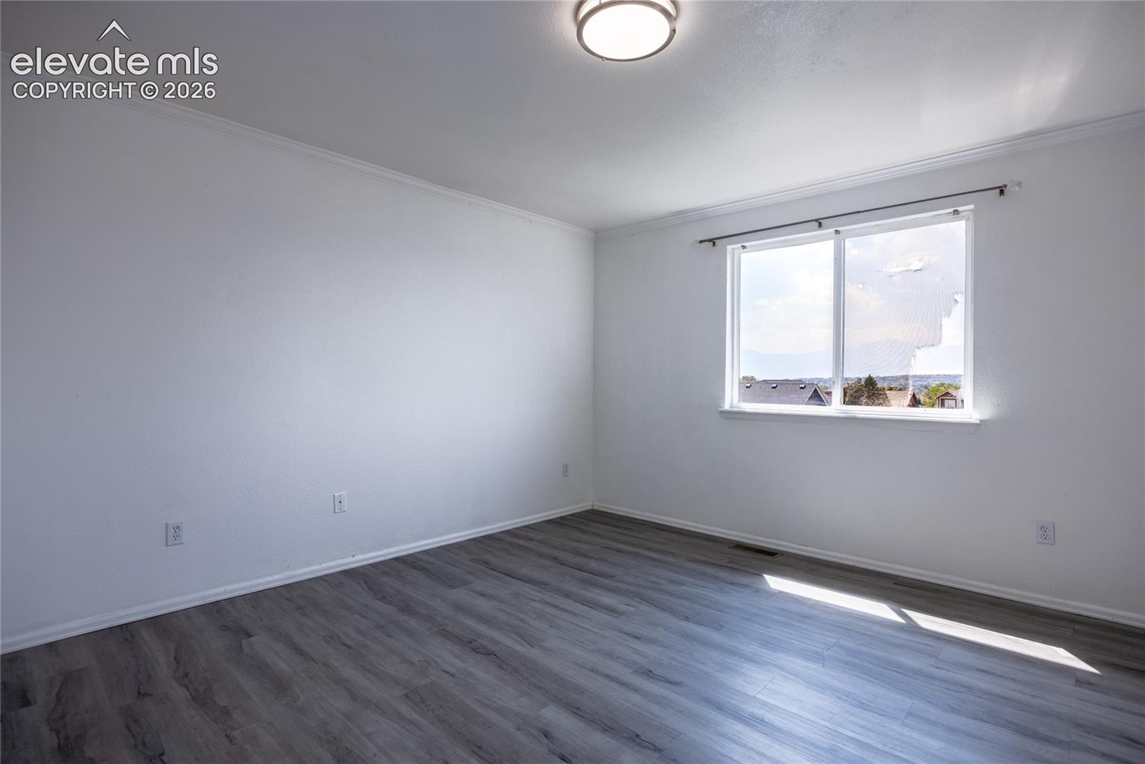 Spacious room featuring wood-finish flooring, white walls, and a large window with a distant landscape