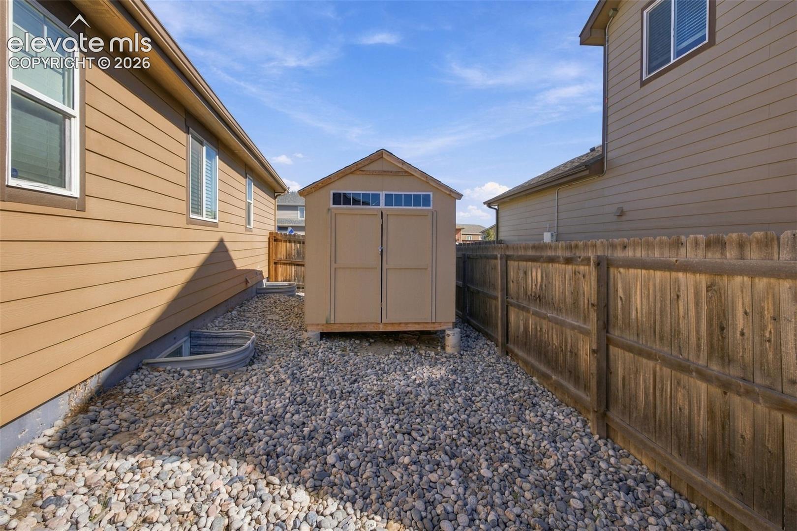 Side yard featuring a detached storage shed, river rock ground cover, and a wood privacy fence