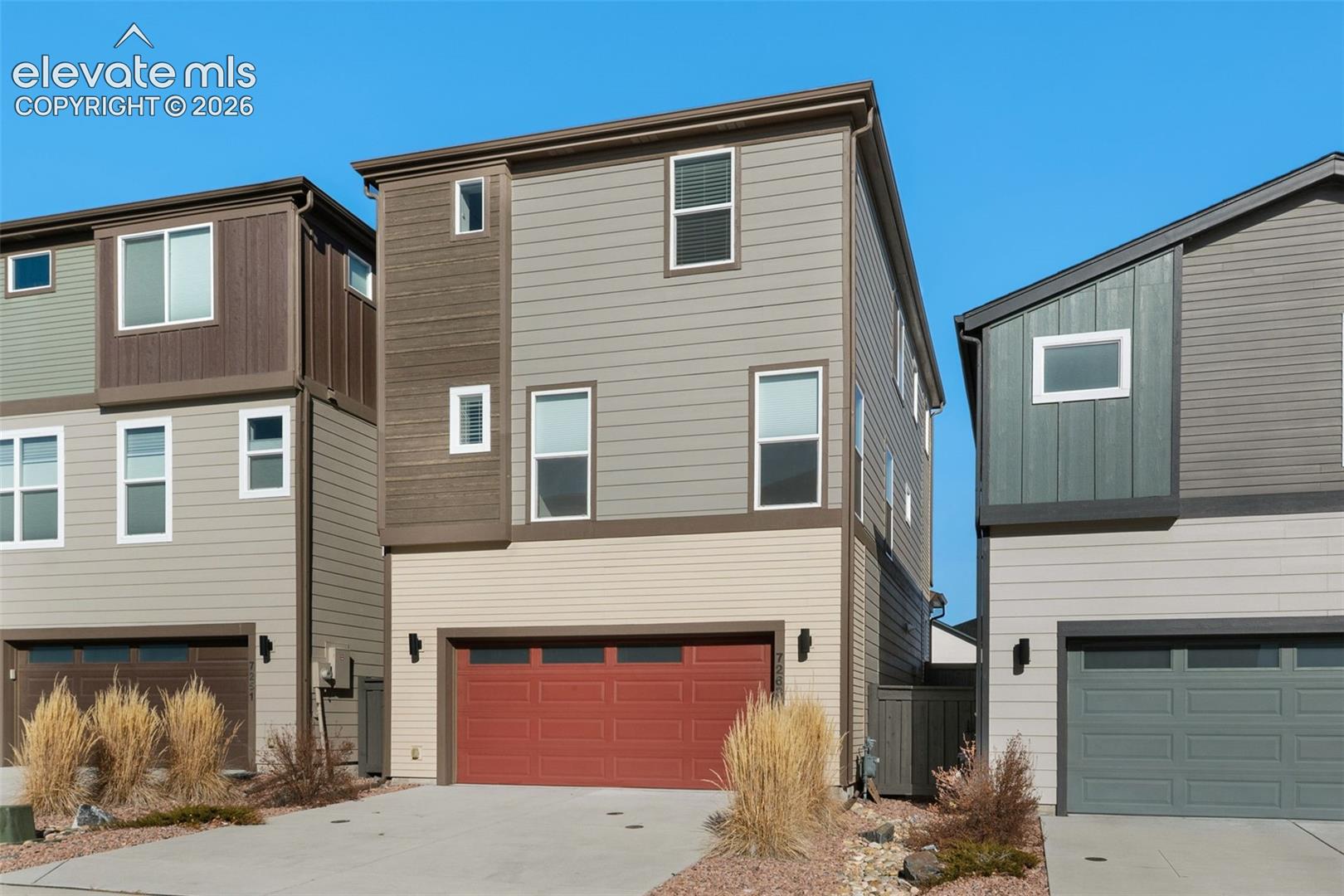 Multi-level townhome exterior featuring varied siding materials and a red garage door