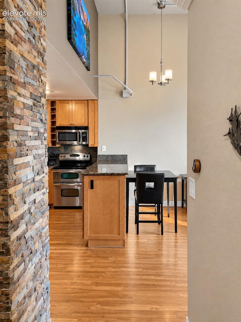 Stone-clad architectural column, wood-finish flooring, kitchen featuring stainless steel appliances, wood cabinetry, and a stone countertop