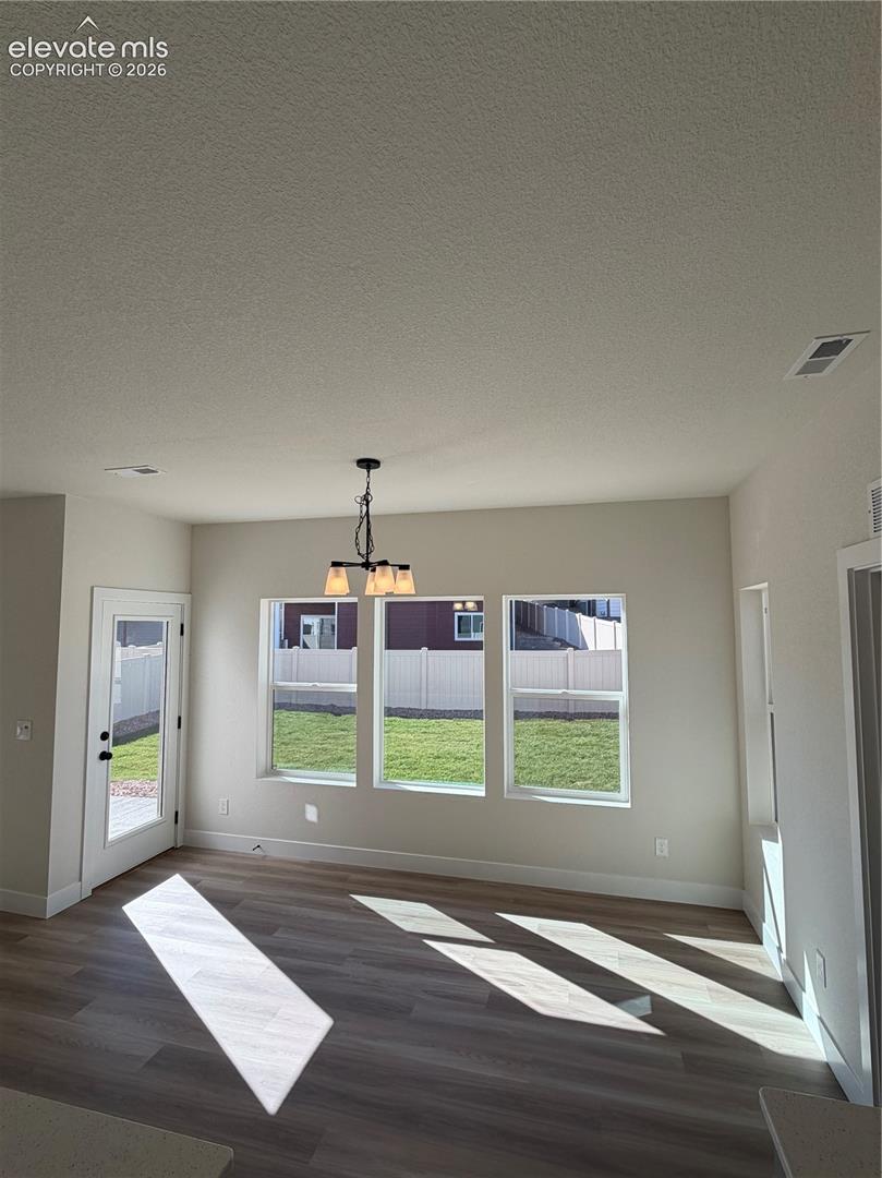 Neutral interior space featuring wood-finish flooring, three large windows, a glass-panel exterior door, and a multi-arm pendant light fixture