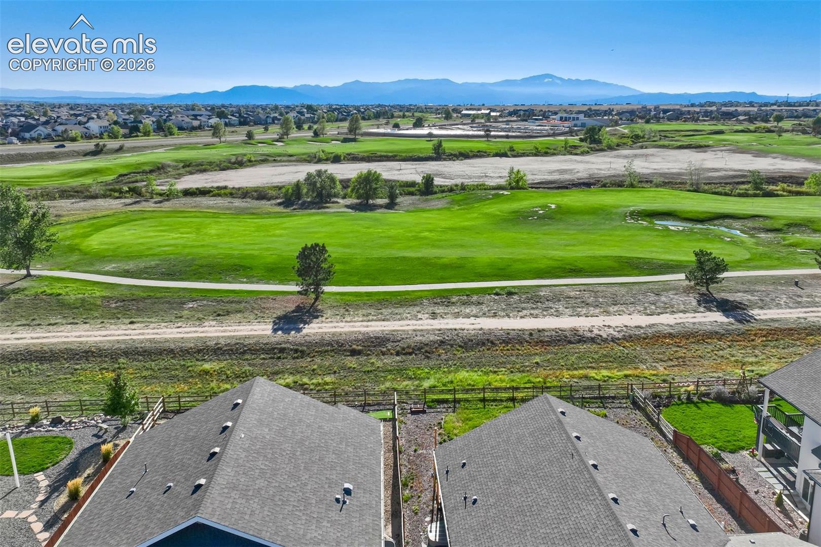 Expansive golf course frontage with established trees, distant mountain range, and residential community