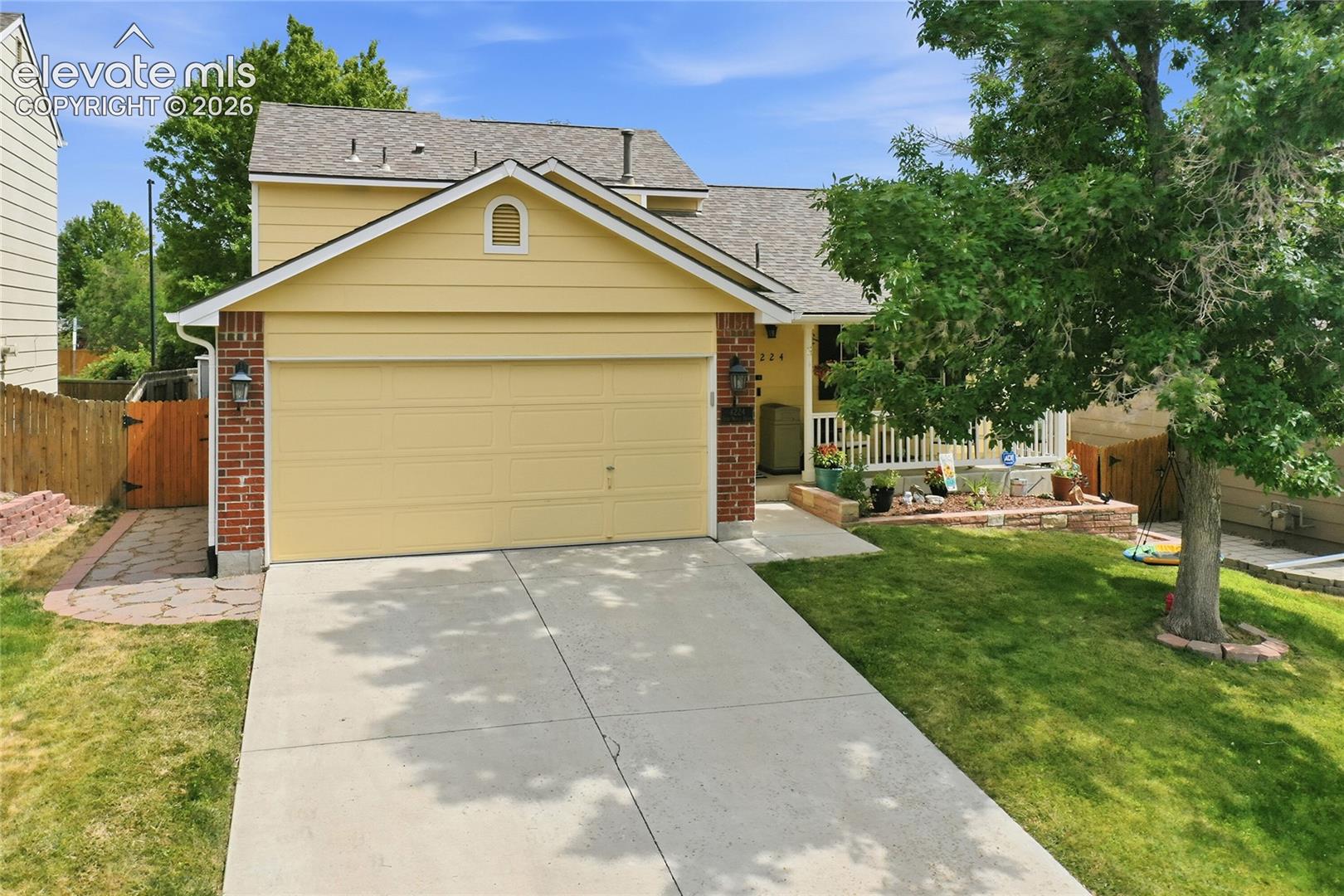 Two-story residence featuring yellow siding, a brick facade, an attached two-car garage, a covered front porch with white railing, and a concrete driveway