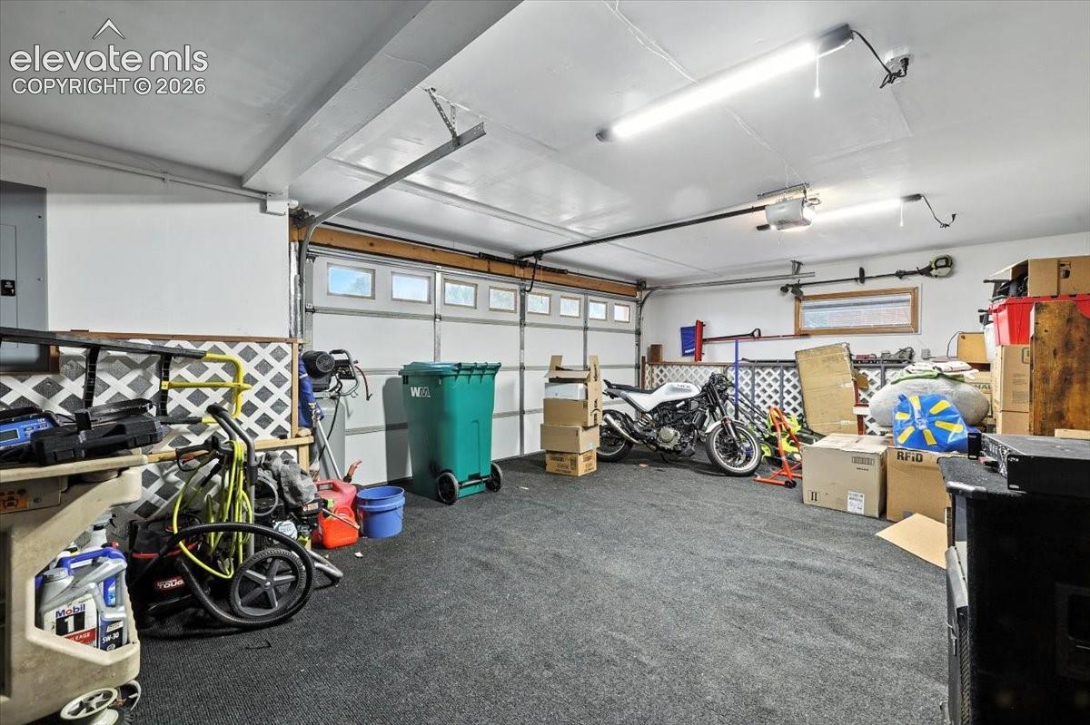Enclosed garage space featuring a multi-panel overhead door, overhead linear lighting, and wall-mounted lattice paneling