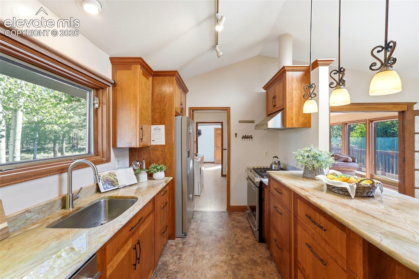 Kitchen featuring wood cabinetry, stainless steel appliances, a vaulted ceiling, and a large window