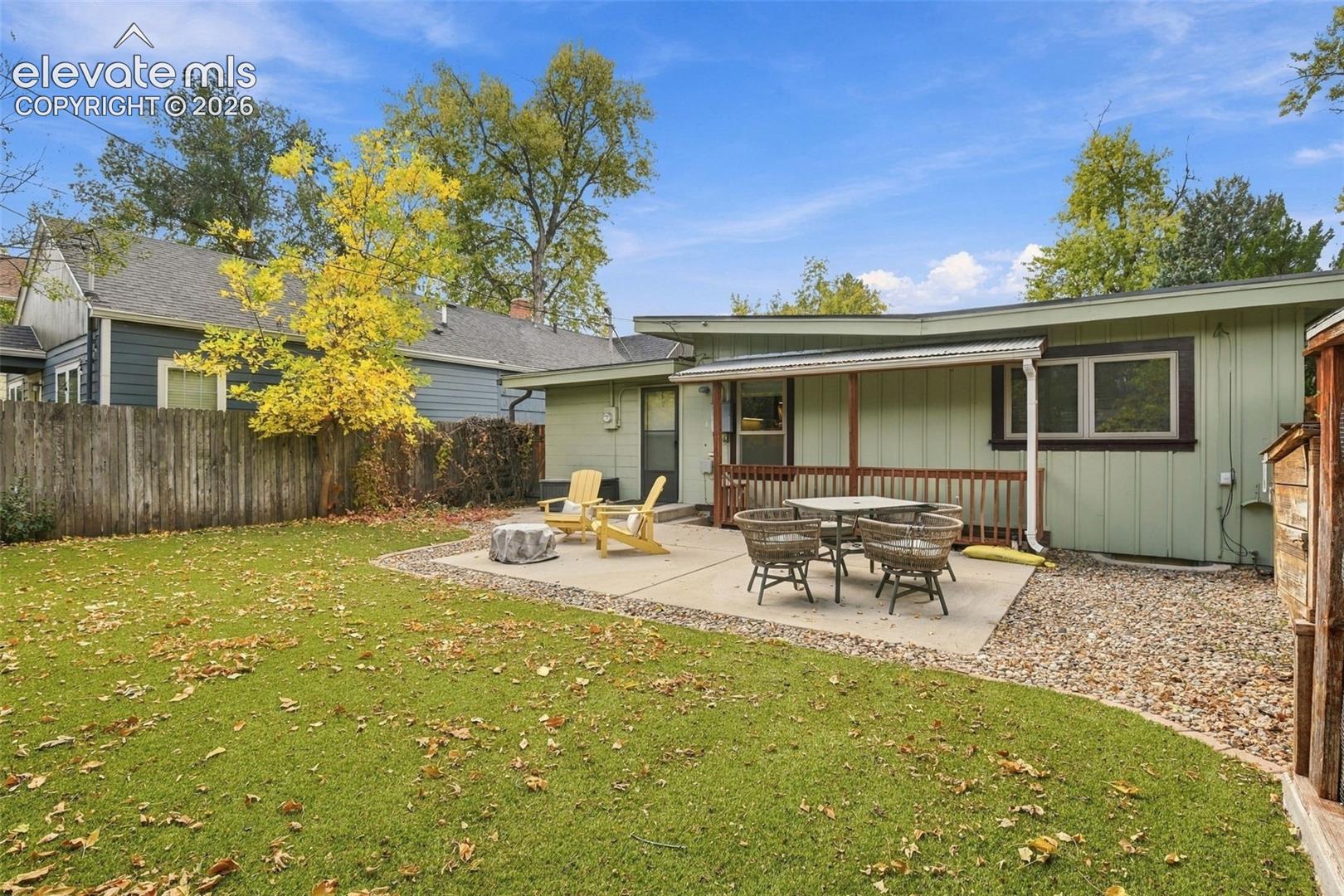 Fenced backyard featuring a concrete patio, covered porch with wood railing, and mature trees