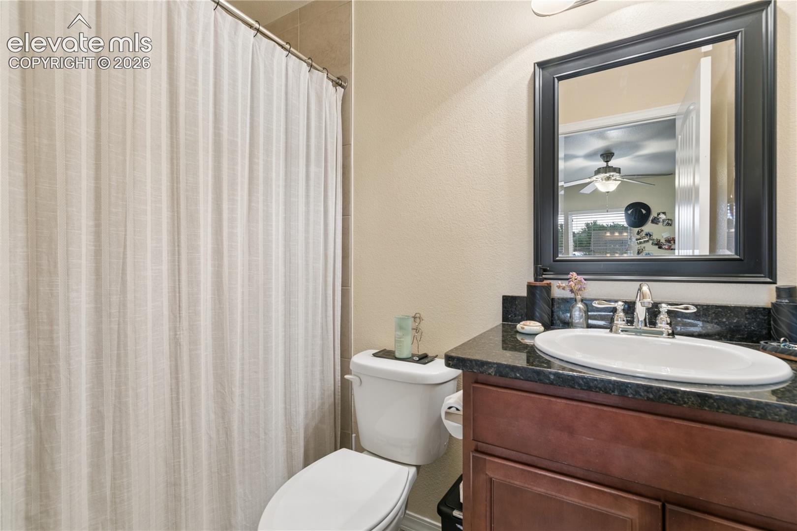 Bathroom featuring a dark wood-finish vanity with a black granite-style countertop, an oval undermount sink, and a framed mirror