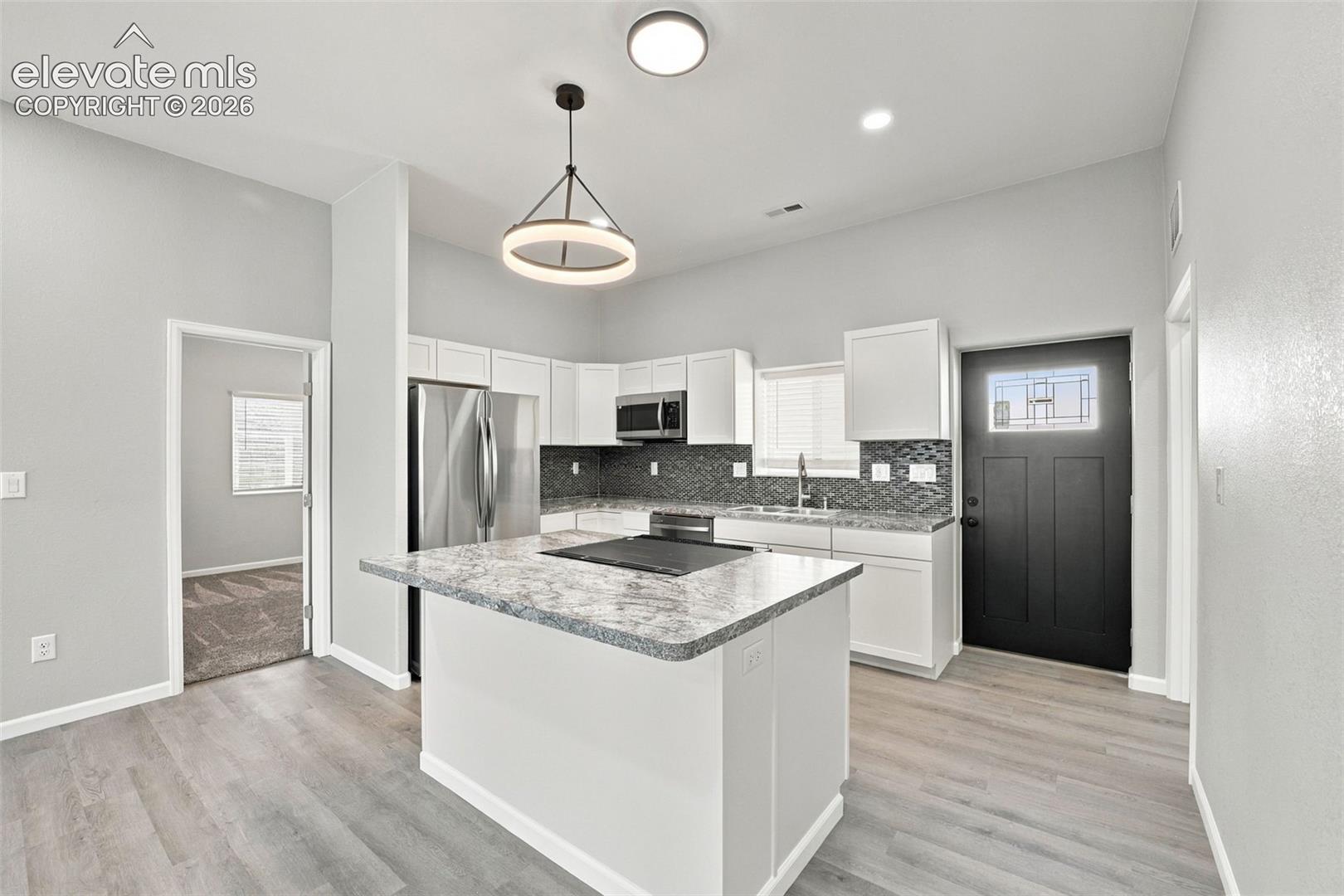 Kitchen featuring white cabinetry, stainless steel appliances, a center island with a stone-finish countertop, and wood-finish flooring
