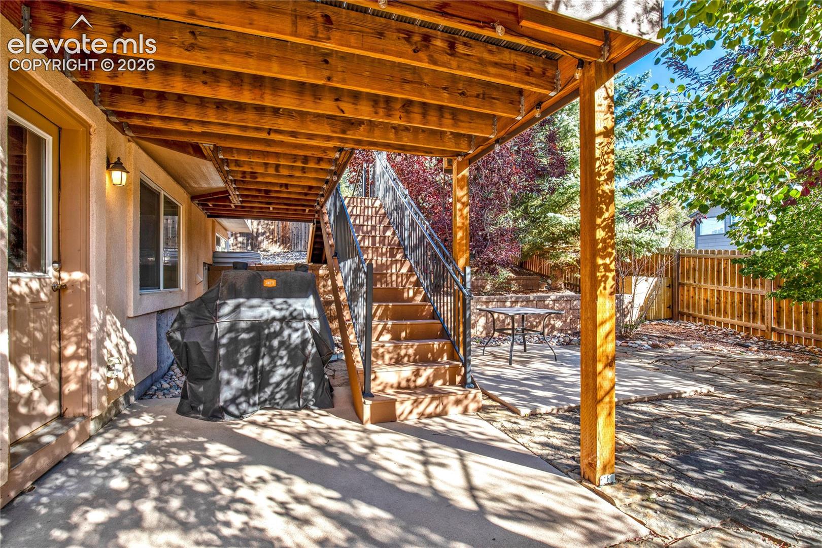 Beneath the elevated deck, the covered flagstone patio creates a shaded outdoor retreat, with stairs connecting to the upper deck + direct access to the backyard.