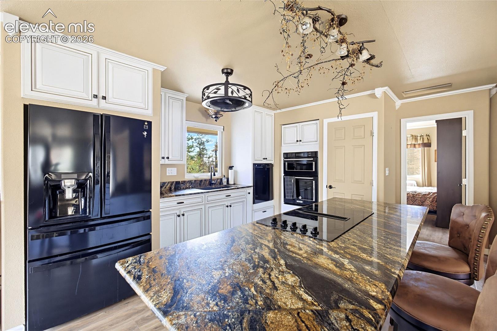 Kitchen featuring custom white cabinetry, dark stone countertops, an expansive center island with an integrated cooktop, a built-in double oven, and a modern drum-style light fixture